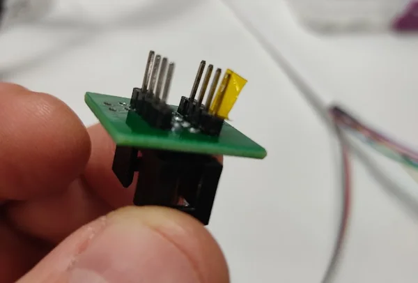 Clip adapter held in hand, with the pin that plugs into the programmer's pin 8 contact covered by a strip of yellow tape